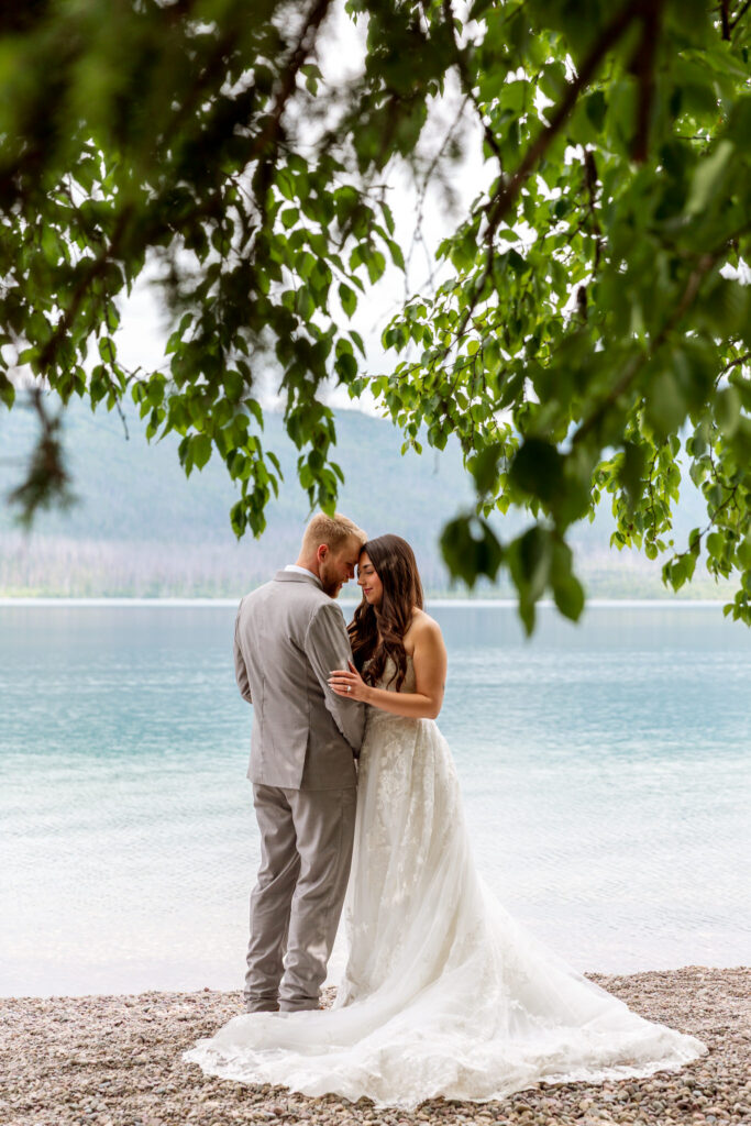 Intimate bride and groom portrait framed by tree branches on the shore of Lake McDonald — Glacier National Park elopement photographer Stacy Edwards Photography