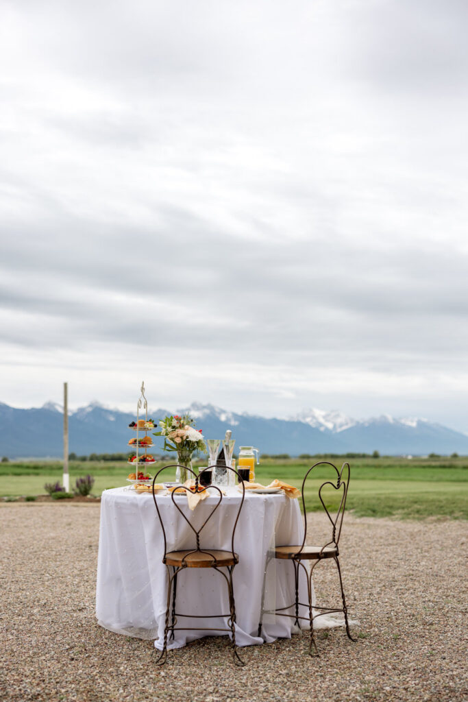 Styled sweetheart table set for two outdoors with tiered dessert stand and Mission Mountains in the background — Micah + Greg — Ember & Altar Wedding — Polson Montana — Stacy Edwards Photography