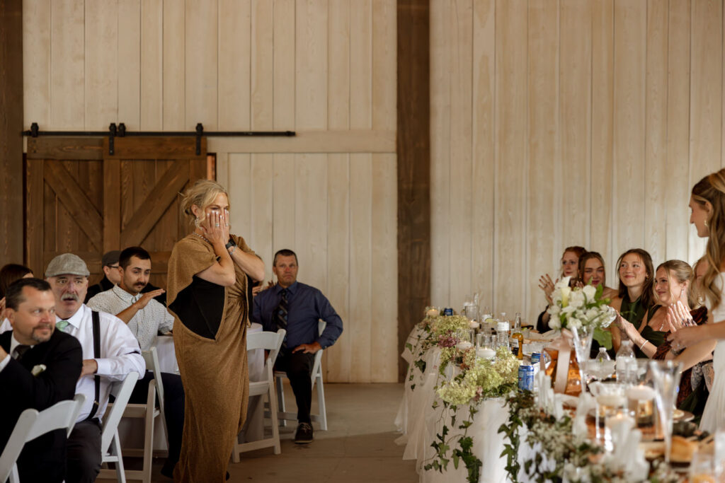 Mother of the bride covering her mouth with emotion during toasts inside the Ember and Altar barn reception — Micah + Greg — Ember & Altar Wedding — Polson Montana — Stacy Edwards Photography