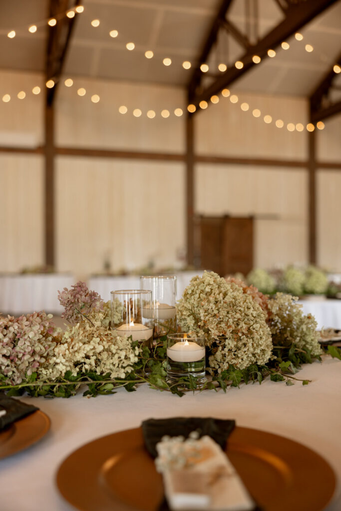 Table detail with lush hydrangea and ivy garland runner, floating candles, and gold charger plates — Micah + Greg — Ember & Altar Wedding — Polson Montana — Stacy Edwards Photography