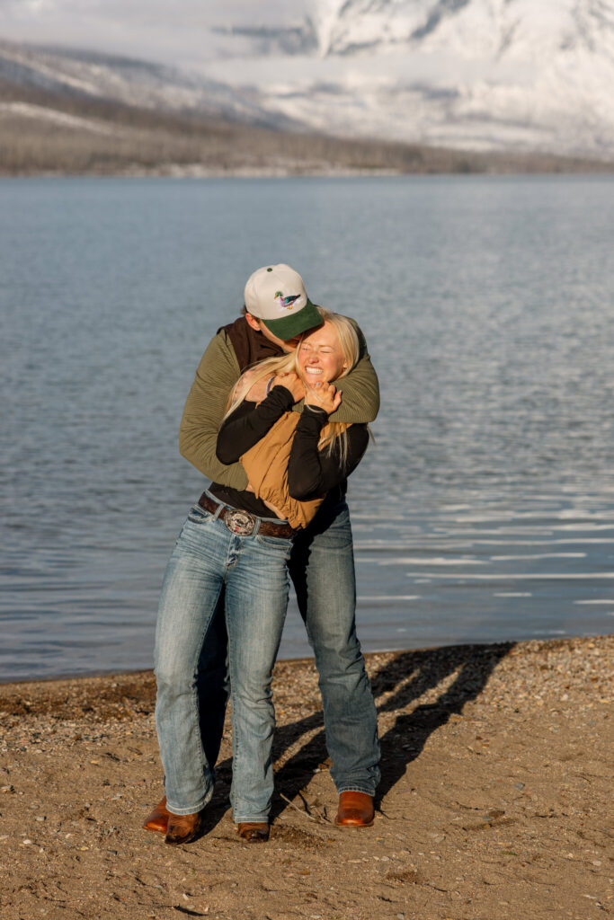 Newly engaged couple laughing and embracing on the shore of Lake McDonald in Glacier National Park — Lindsey and Ethan — Sandy Point Glacier National Park Engagement Photographer — Stacy Edwards Photography