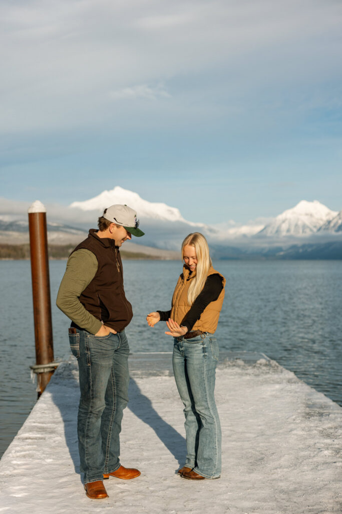 Newly engaged couple admiring the engagement ring together on a snowy dock at Lake McDonald — Lindsey and Ethan — Apgar Village Glacier National Park — Stacy Edwards Photography