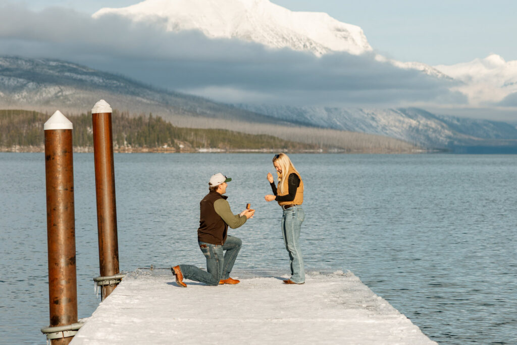 Woman raising her hand in disbelief as her partner proposes at Apgar Village on Lake McDonald — Lindsey and Ethan — Glacier National Park Proposal Photographer — Stacy Edwards Photography