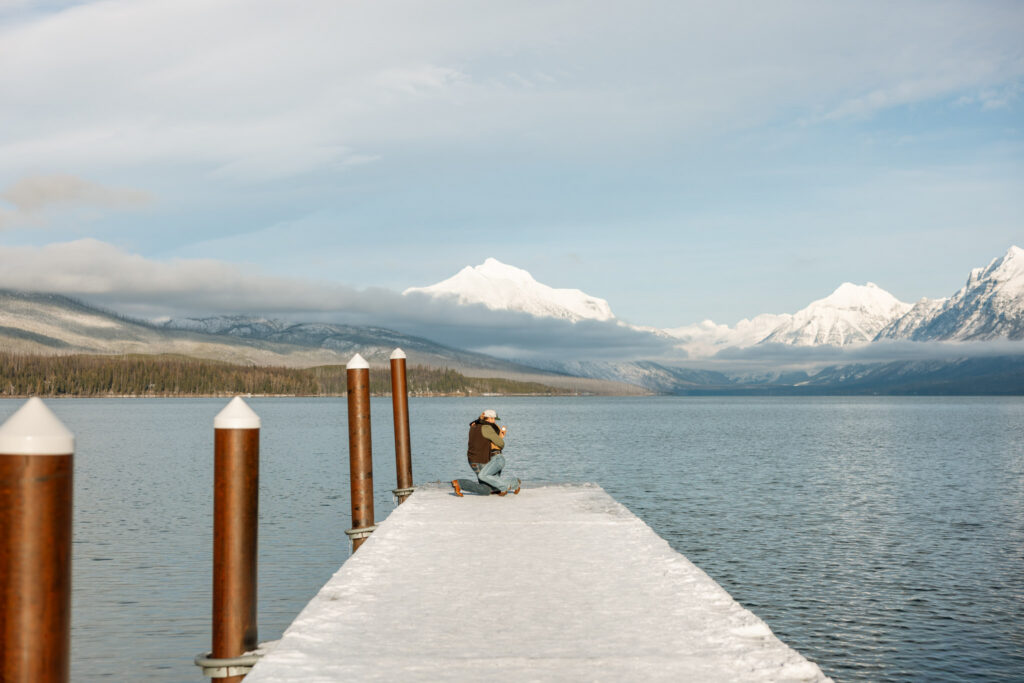 Newly engaged couple embracing at the end of a snow-covered dock surrounded by Glacier National Park mountains — Lindsey and Ethan — Lake McDonald Apgar Village — Stacy Edwards Photography