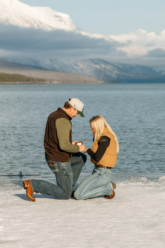 Newly engaged couple both kneeling on the dock admiring the engagement ring at Lake McDonald — Lindsey and Ethan — Apgar Village Glacier National Park — Stacy Edwards Photography